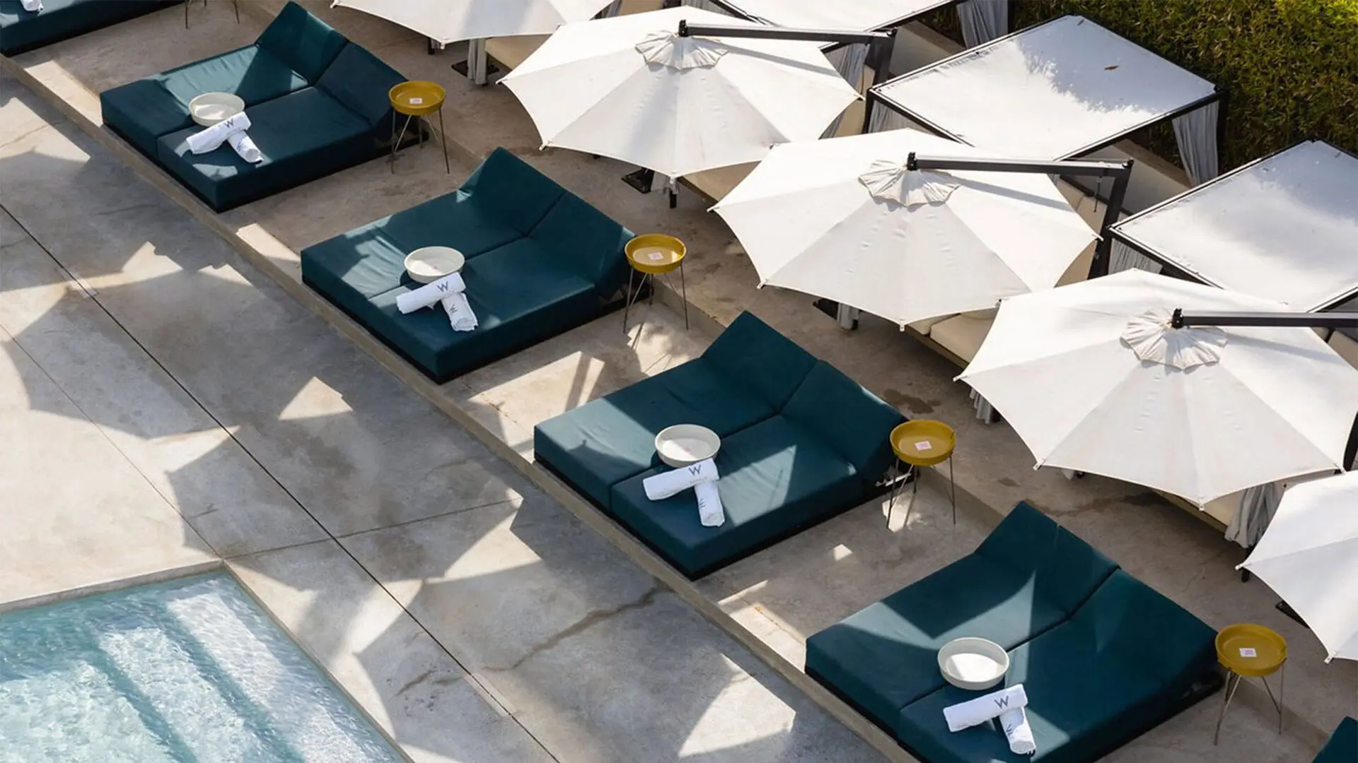 Parasoles crean sombra sobre camas al borde de una piscina en hotel de alta gama con sombrillas Fim Umbrellas