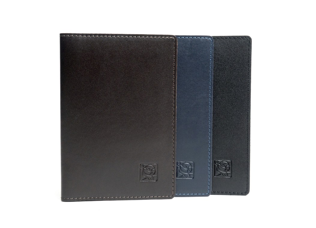 Three smooth leather passport covers standing upright side-by-side in dark brown, navy blue, and black.