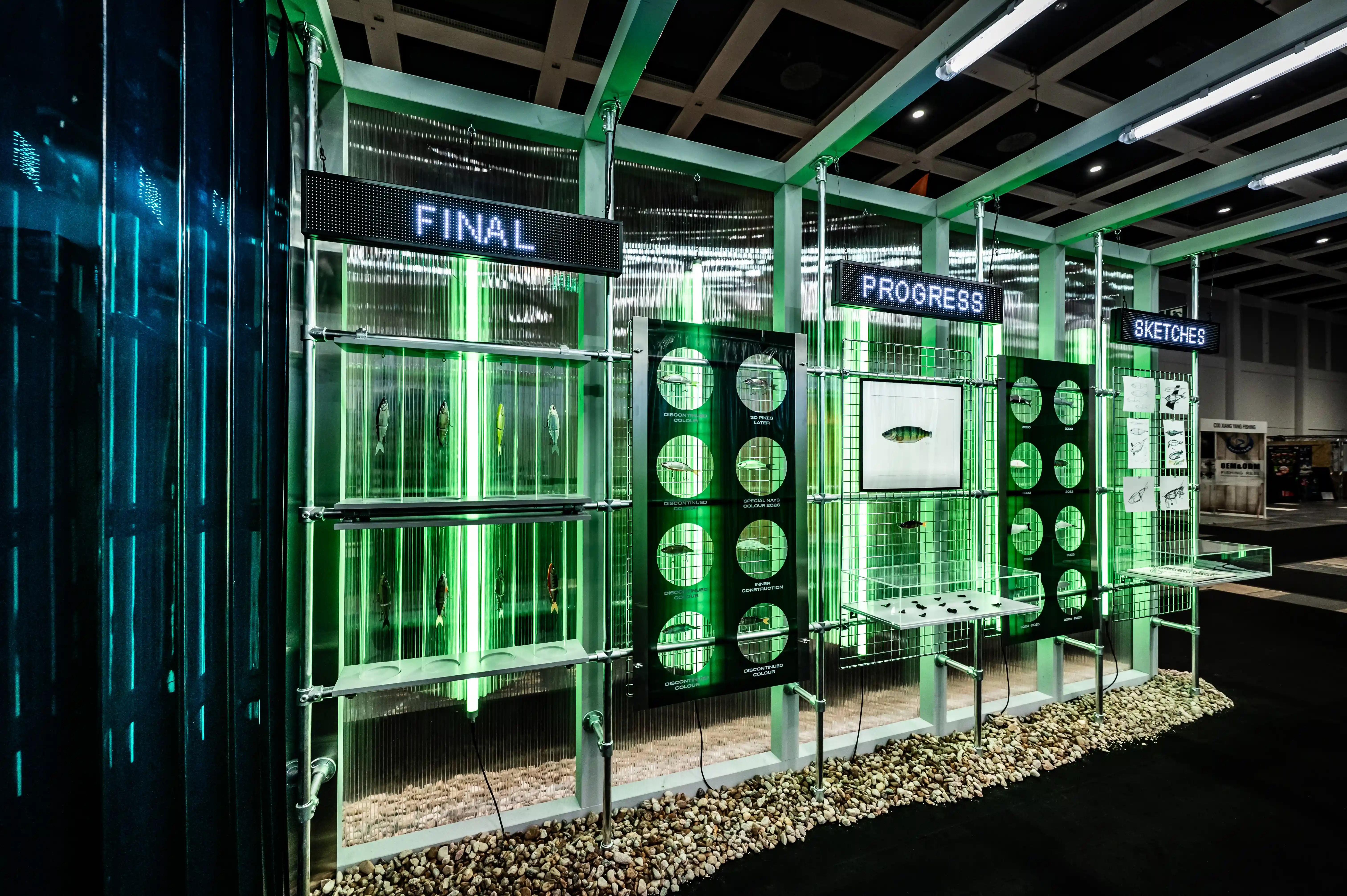 Glass lab wall at the Nays booth with green-lit displays for sketches, progress and final lure stages on pebbles.