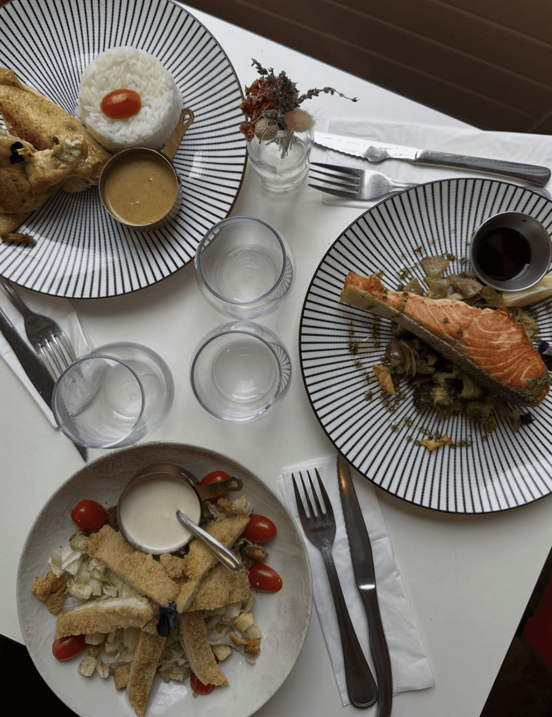 Plate with a seared salmon fillet topped with green herb garnish and sauce, served on a white dish placed on a dark green marble table beside a white candlestick.
