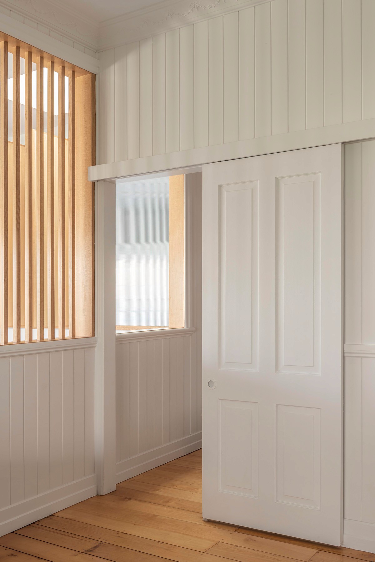 Refined interior detail with sliding panel door, vertical timber screen, and restored Queenslander wall lining.