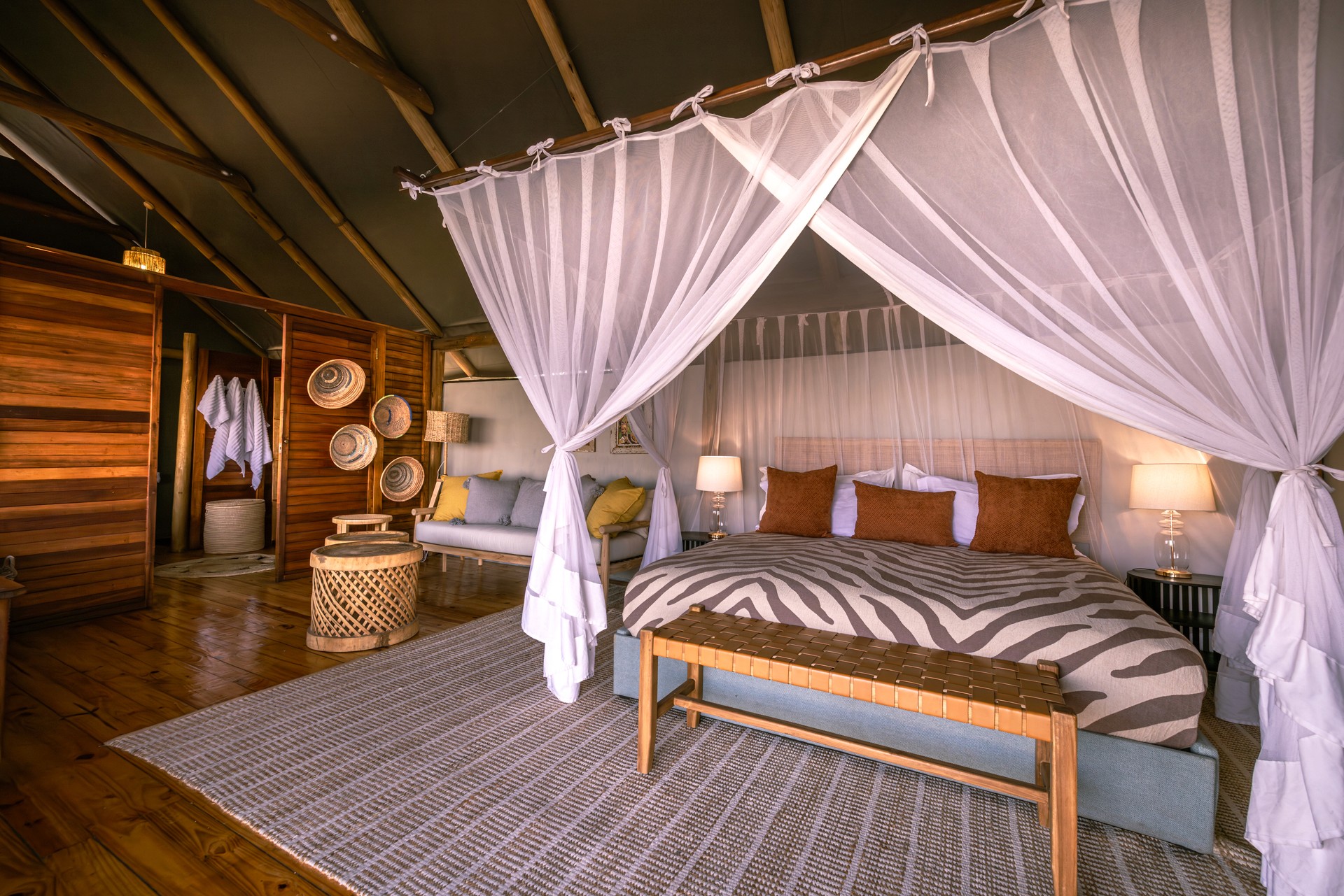 Kujwana Delta Ride, Okavango Delta Botswana. Riverside Suites på Kujwana Camp. Närbild på säng i lyxigt boende med utsitk över Okavango. Stor dubbelsäng vackert bäddad omgiven av myggnät.