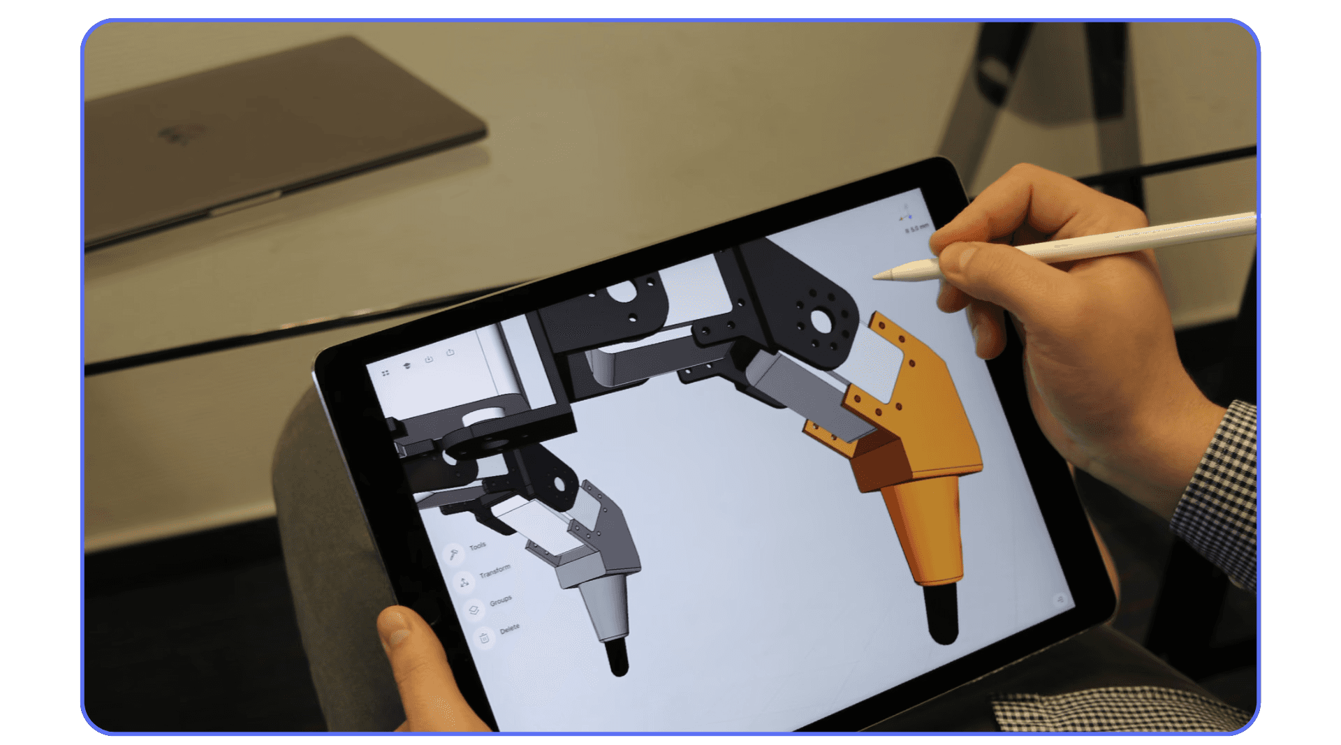 A person using an Apple Pencil to design a mechanical arm with orange and gray components on a 3D CAD modeling app displayed on an iPad.