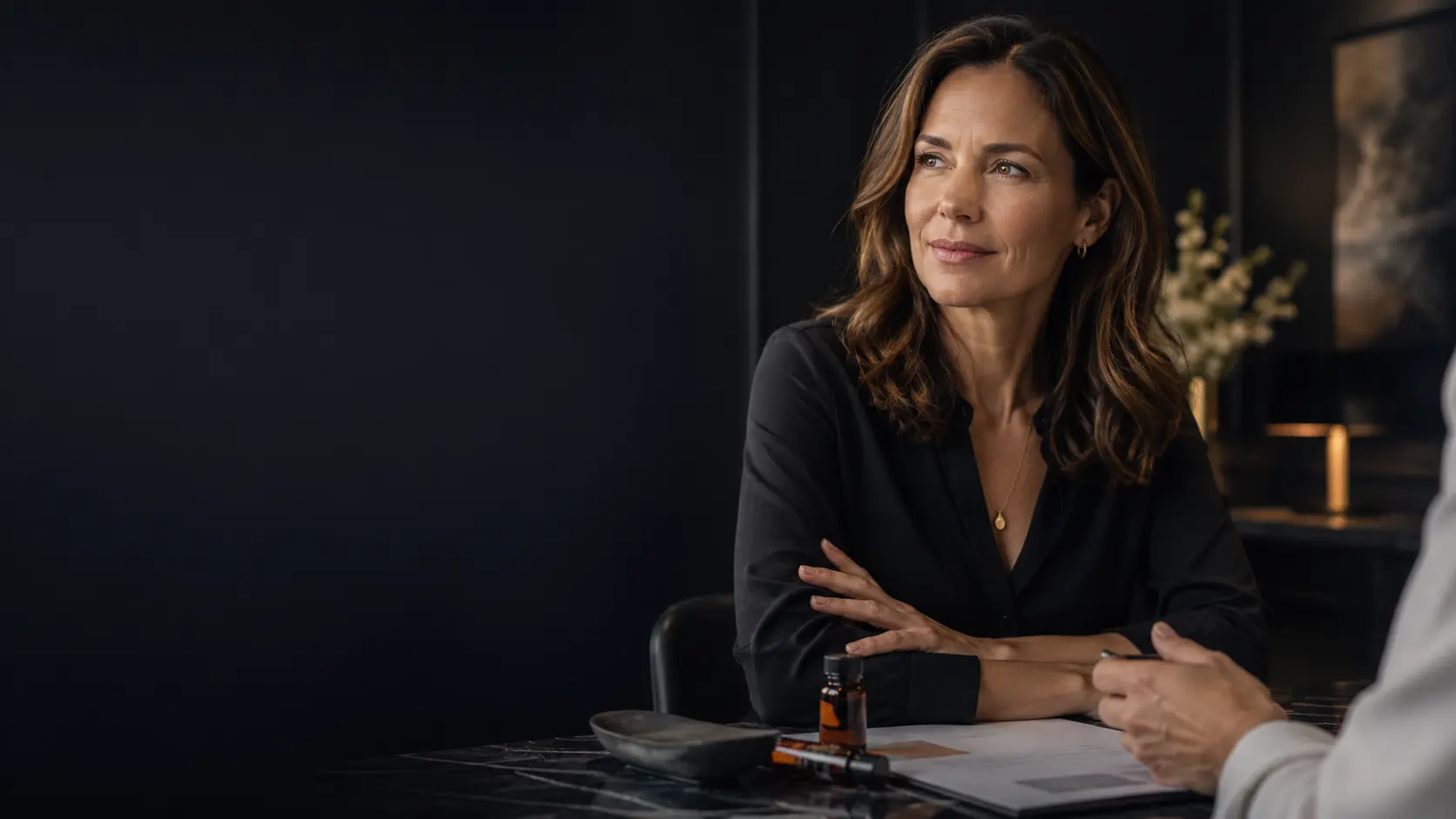 Woman with arms crossed seated at a table in a dim room