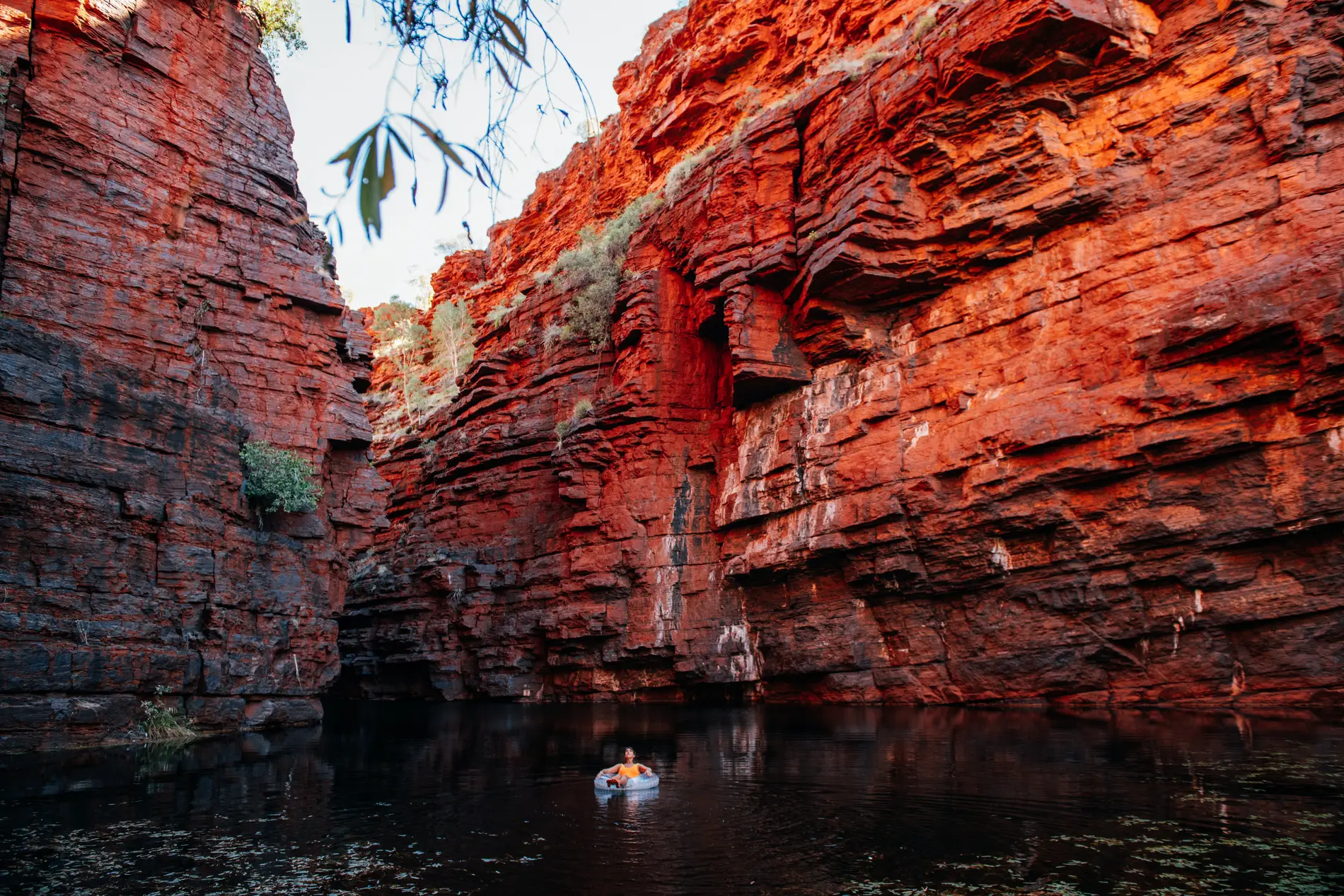 A red-walled gorge with a still pool below, a swimmer floating on the water