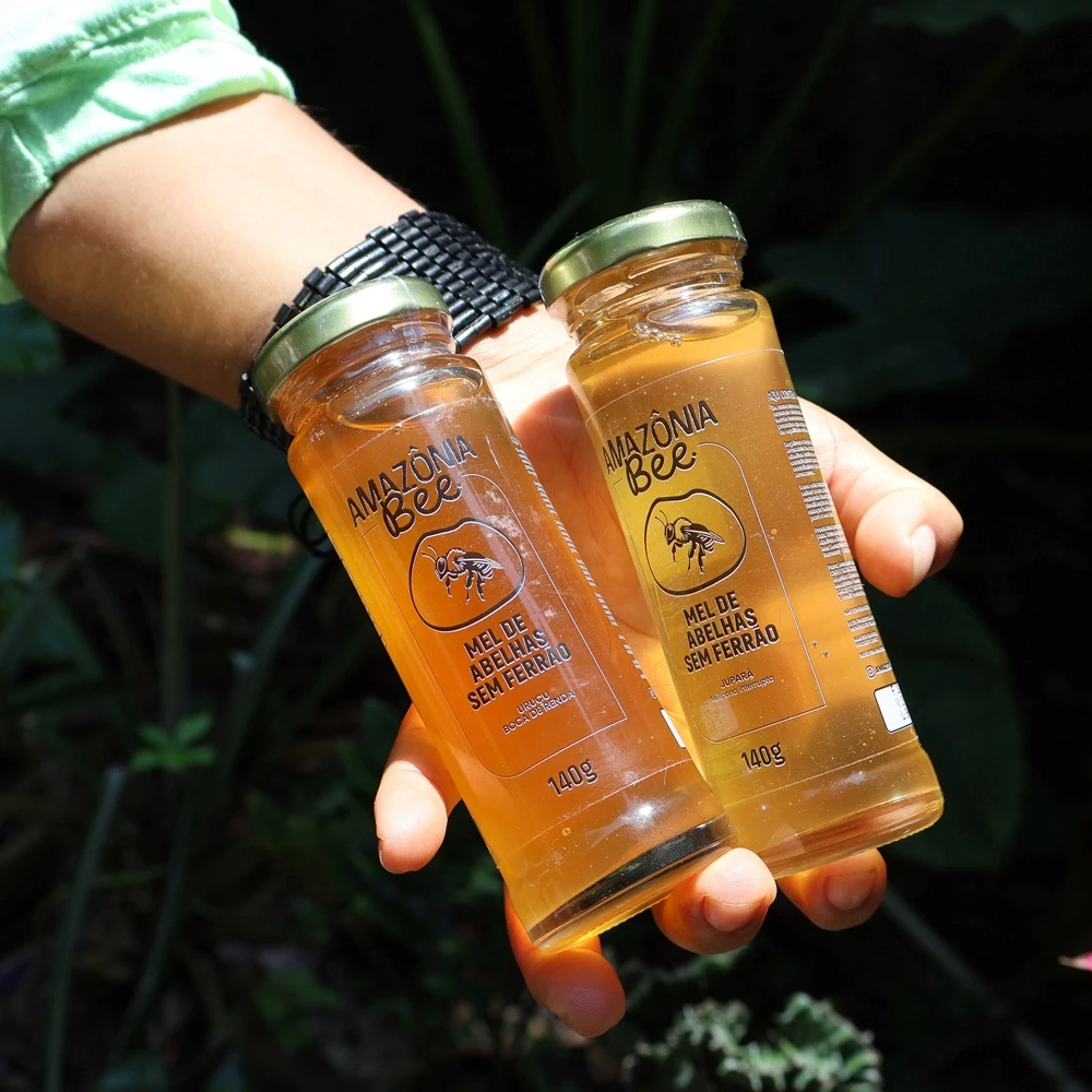 Mão segurando garrafas de mel sem ferrão.