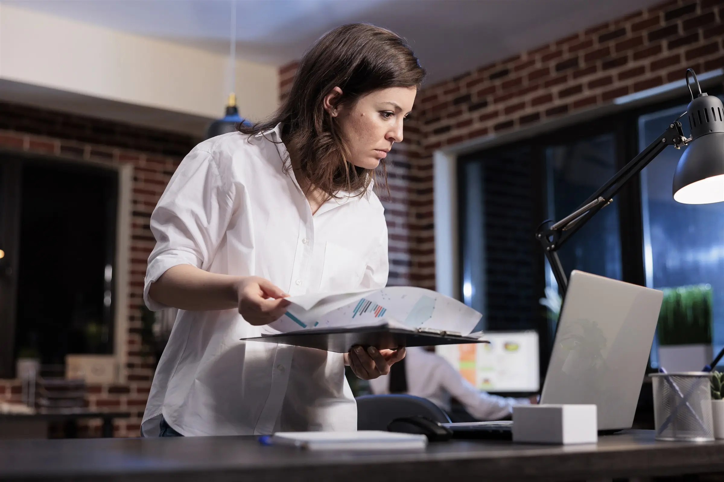 Team member handling a stack of paper documents next to a laptop, KGT Solutions