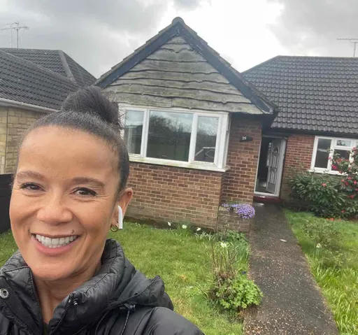 Woman with short hair smiling in front of a brick house with a bay window
