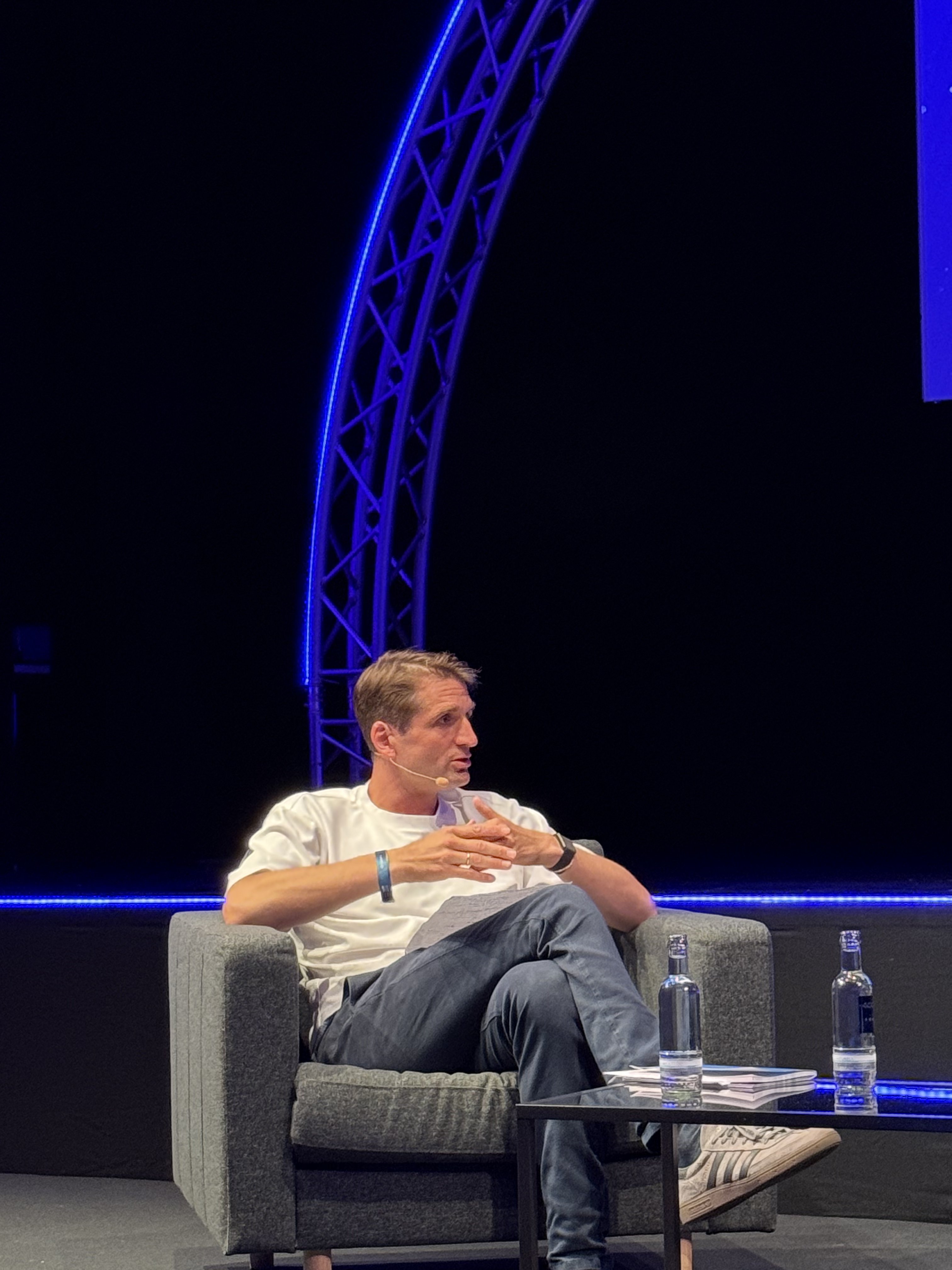 A smiling woman with her arms crossed, standing against a dark green background. She has long, dark hair.