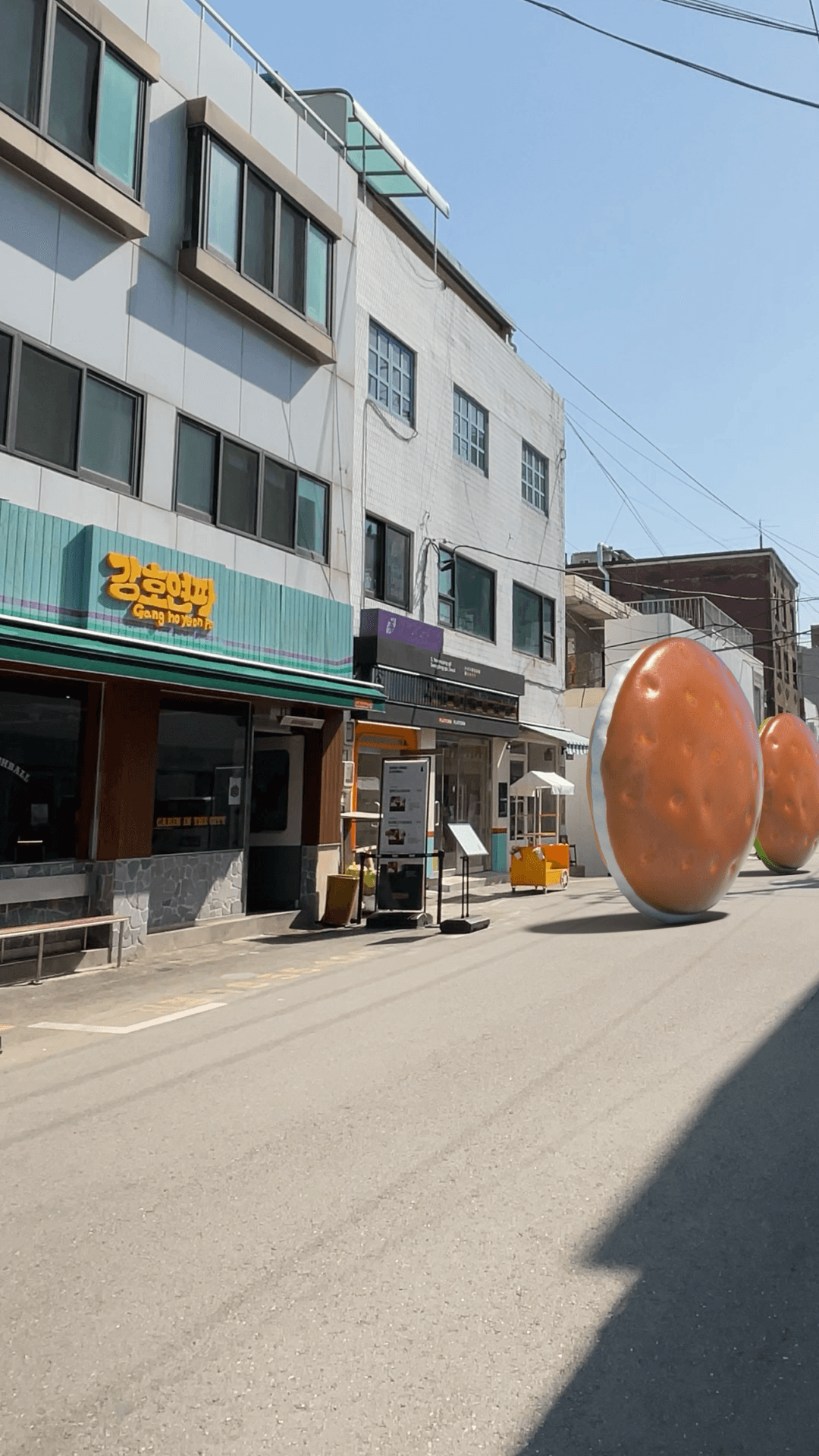 거대한 삼립 크림빵들이 성수동 골목을 가로질러 크림 아뜰리에 팝업스토어로 굴러가는 FOOH 장면