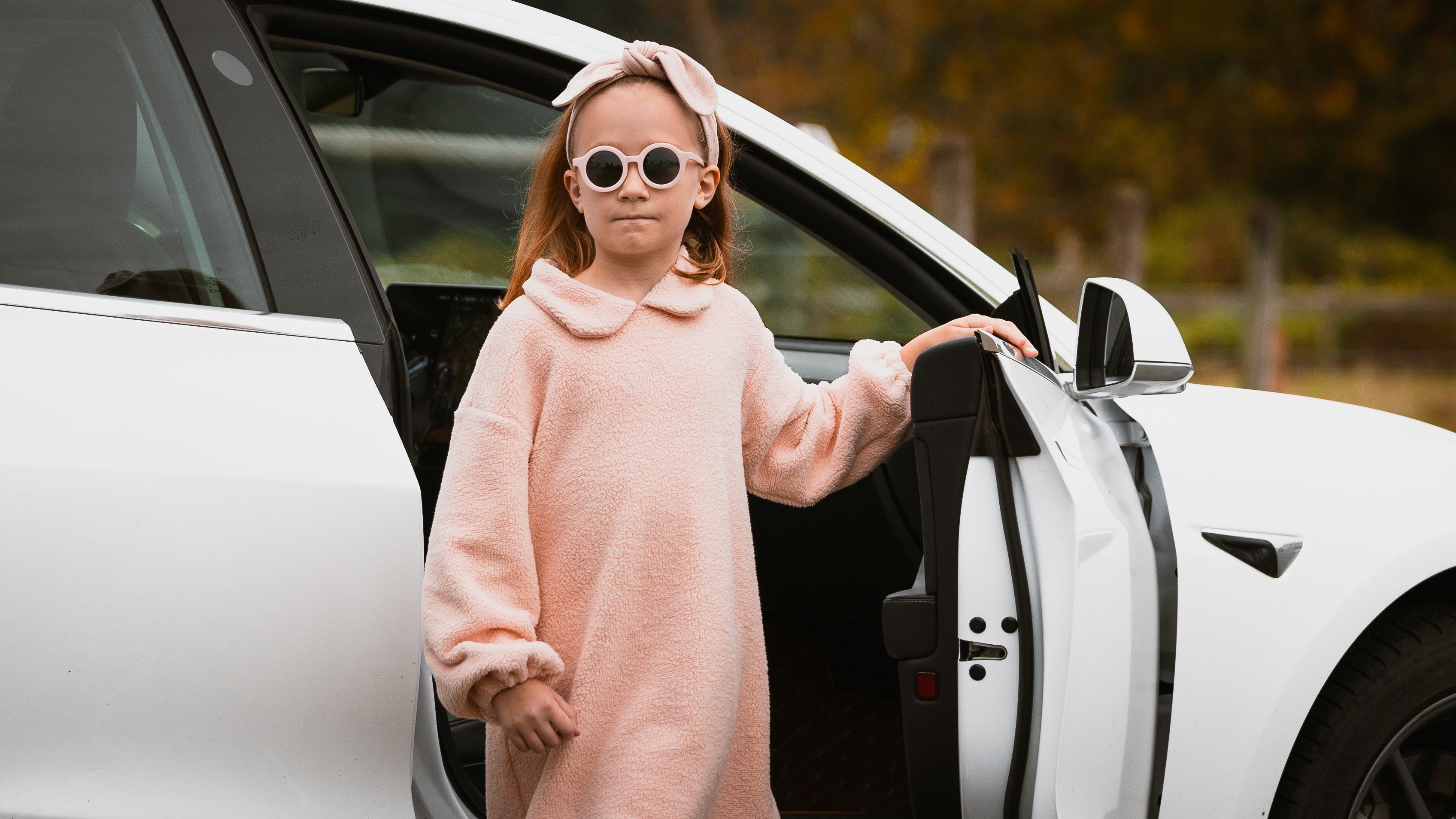 Girl in a pink sweater dress and round sunglasses stepping out of a white car