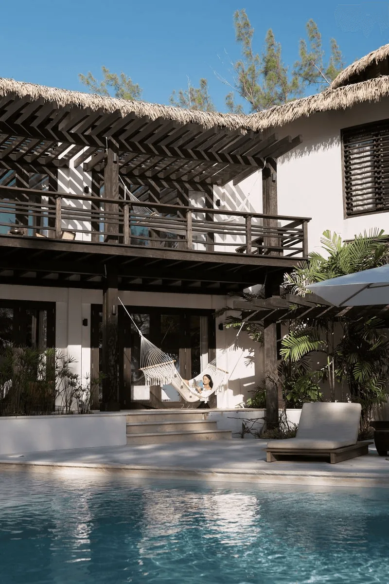 A modern villa featuring a patio, pool, and lush greenery under a clear blue sky.