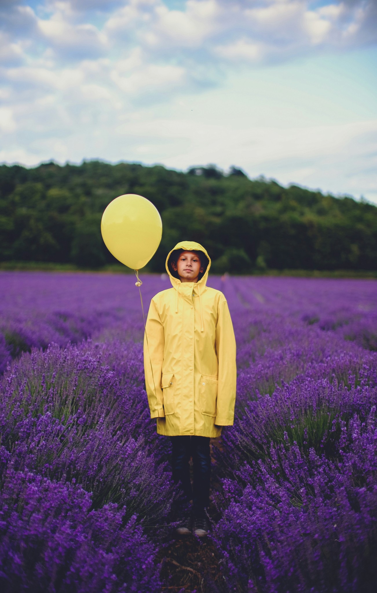 human standing in a purple garden wearing a yellow vest and holding a yellow balloon