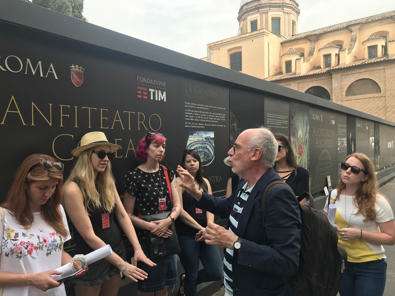 A photo of a teacher talking to the students while they stand in front of some wall exhibition.