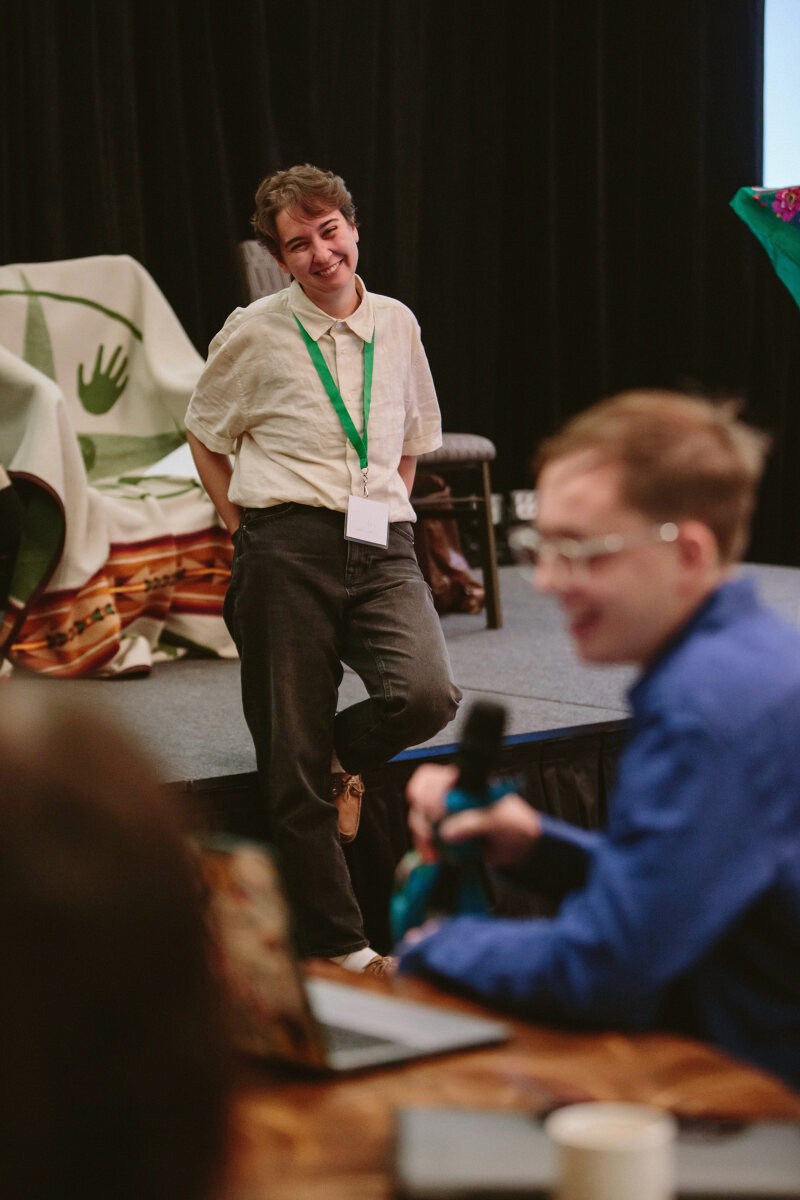 A speaker presents on stage while an audience member sits attentively, engaged in the discussion.