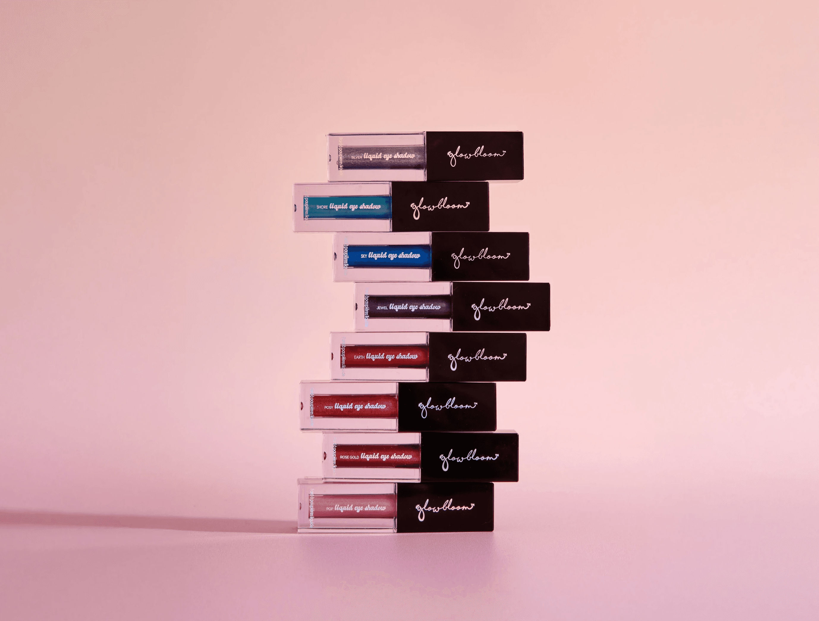 A stack o lipgloss on a pink gradient background.