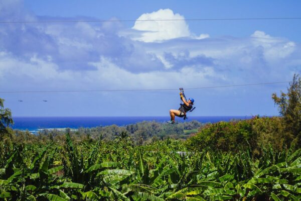 woman ziplining in oahu with an ocean view across the jungle