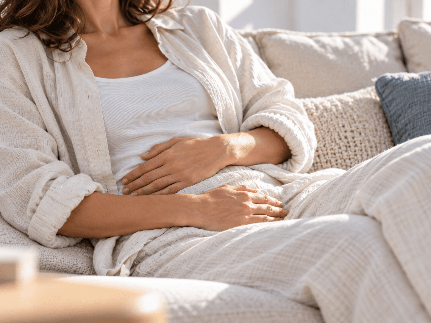 Woman seated on a sofa, resting her hands on her abdomen