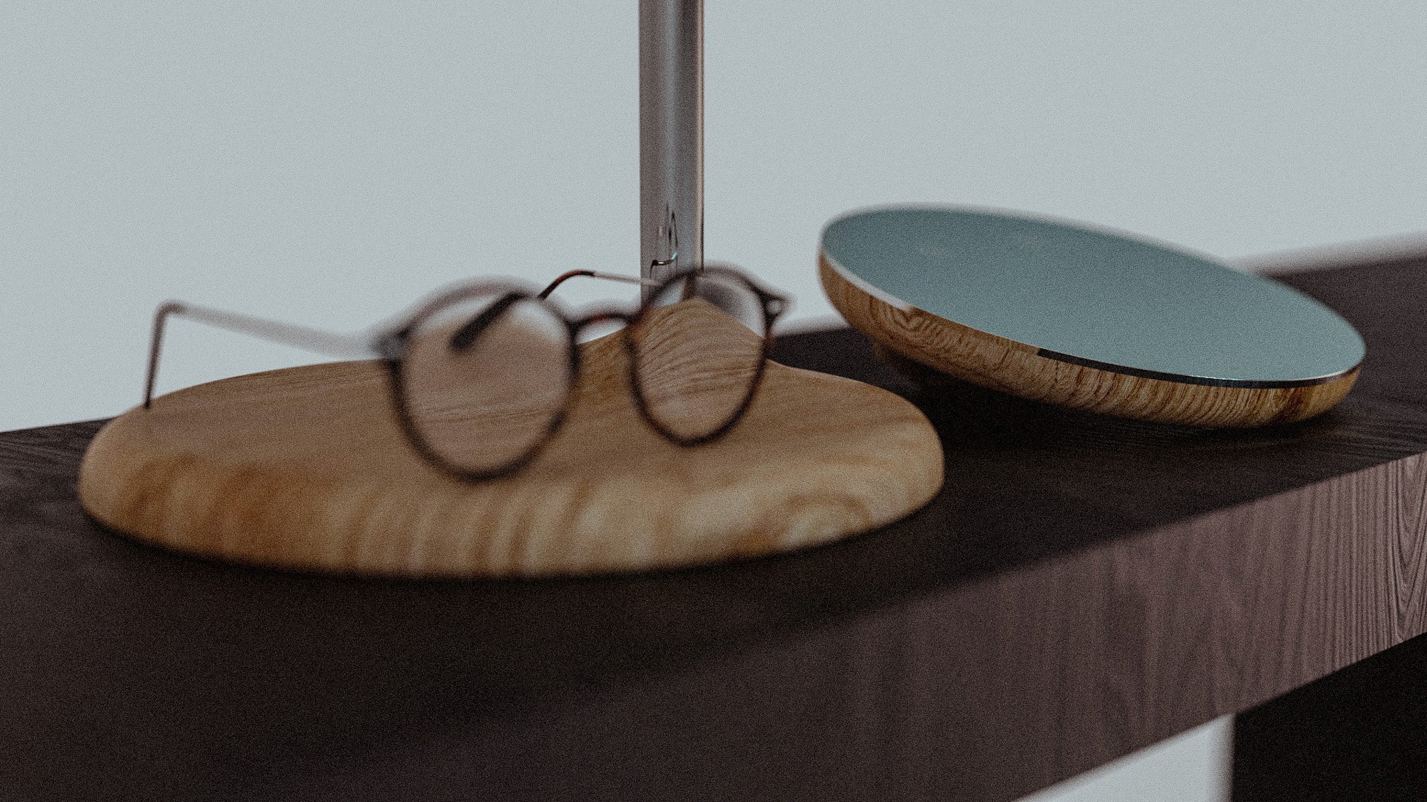 A pair of round-framed glasses rests on a wooden desk organizer beside a sleek, modern mirror.