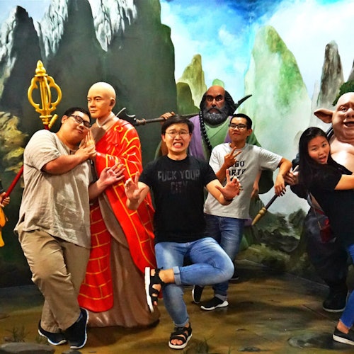 人们在山和天空背景下,以幽默的姿势与真实的僧人雕像和神话角色合影。