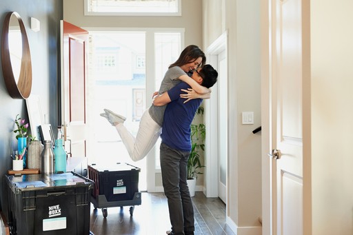 A person joyfully embraces another in a bright, modern home setting, conveying warmth and connection.