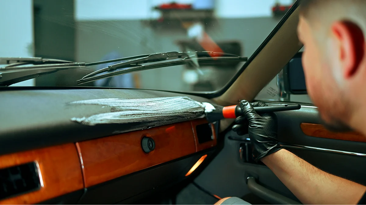 Technician cleaning a vehicle dashboard with a detailing brush