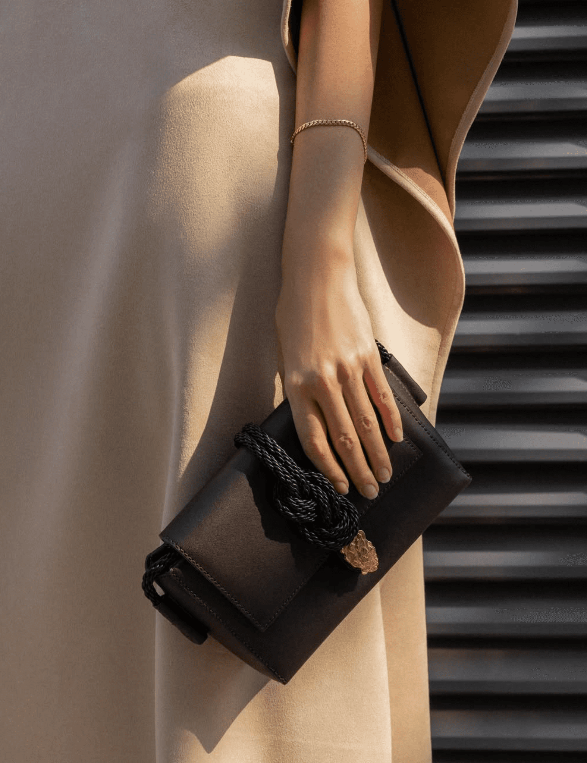 Close-up of a woman in a sleeveless beige pleated dress wearing a sculptural brown leather belt bag tied at the waist, with testimonial quote overlay.