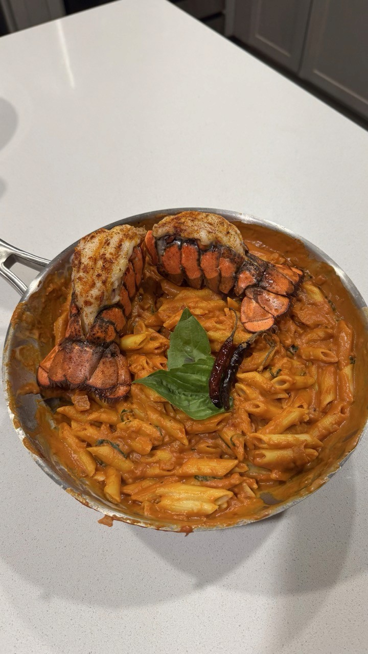 Skillet of creamy tomato penne vodka pasta topped with two lobster tails and basil – elevated lobster pasta date night recipe Wellness by Suhey