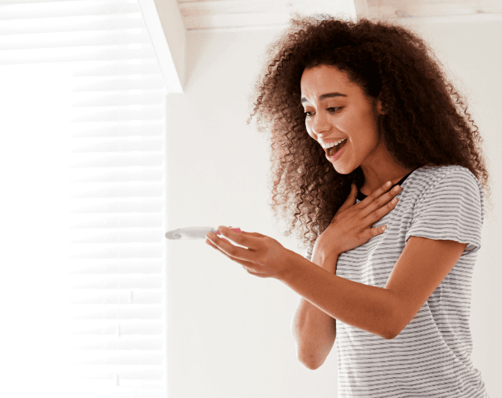 Woman looking happily at a pregnancy test, representing fertility health insurance benefits