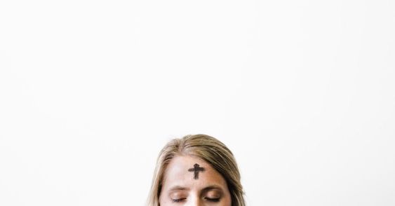 A person with a small ash cross on their forehead and eyes closed