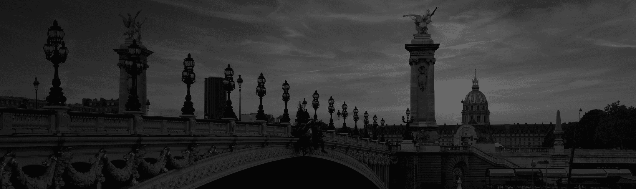 Black and white photo of Pont Alexandre III in Paris, France. Two people walk across the bridge.