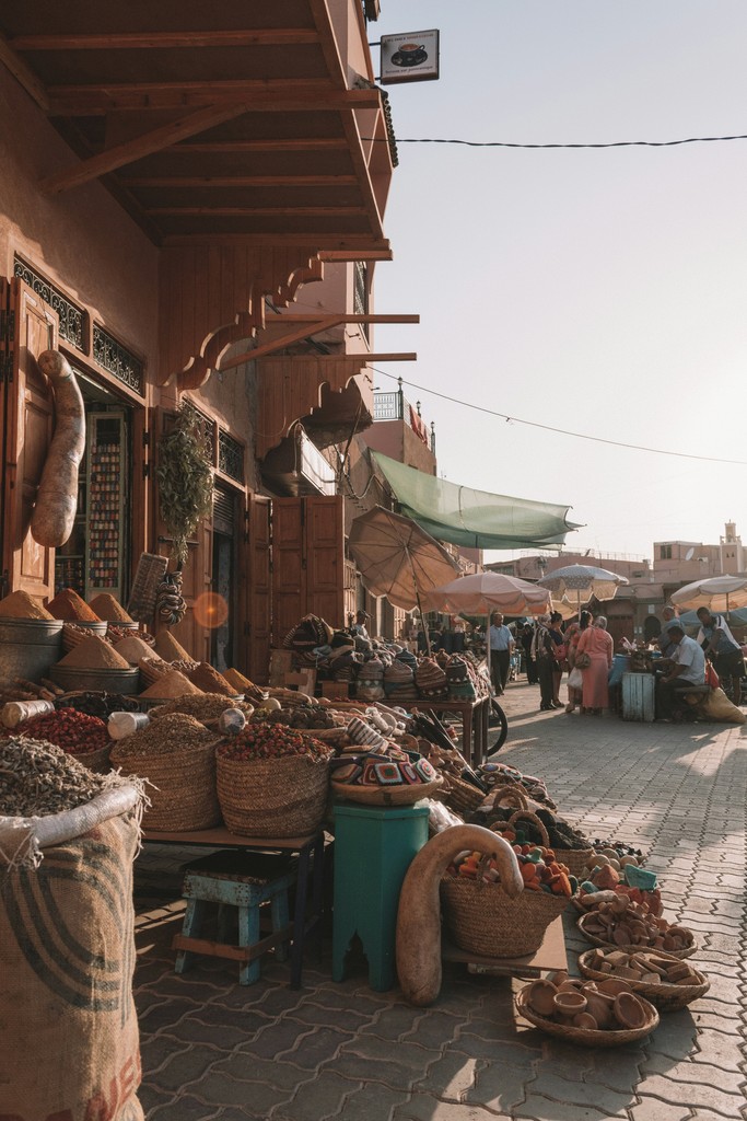 A bustling Moroccan street market in the warm evening light, with vibrant displays of spices, woven baskets, and handcrafted goods, capturing the rich culture and lively atmosphere of the local marketplace.