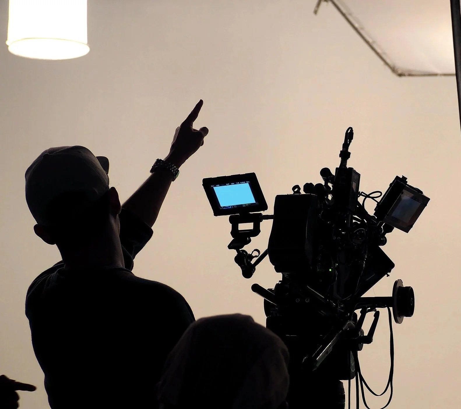 A silhouetted crew member gesturing beside a studio camera rig and monitors.