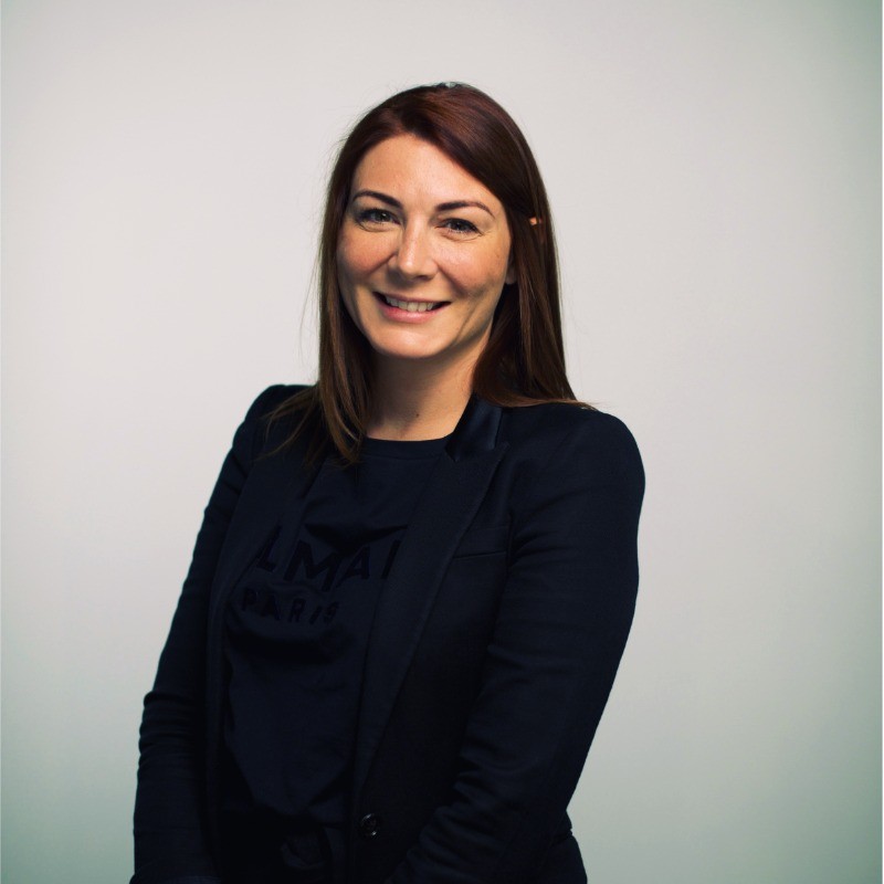 A smiling person wearing glasses and a patterned shirt stands against a plain white background.
