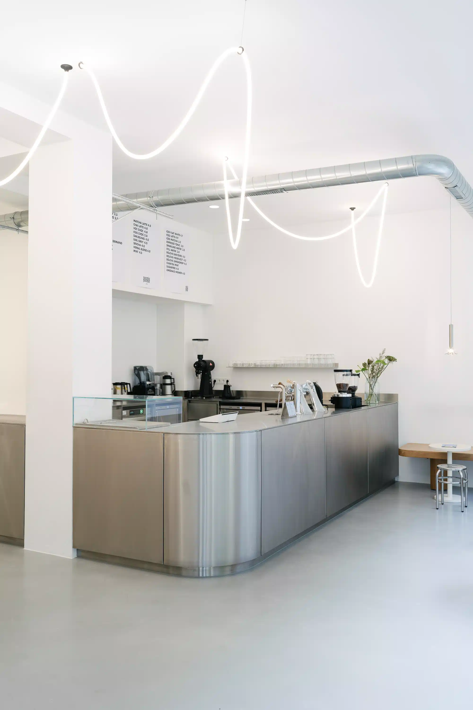 Reforma – minimalist coffee bar counter in brushed stainless steel with organic neon light installation on the ceiling