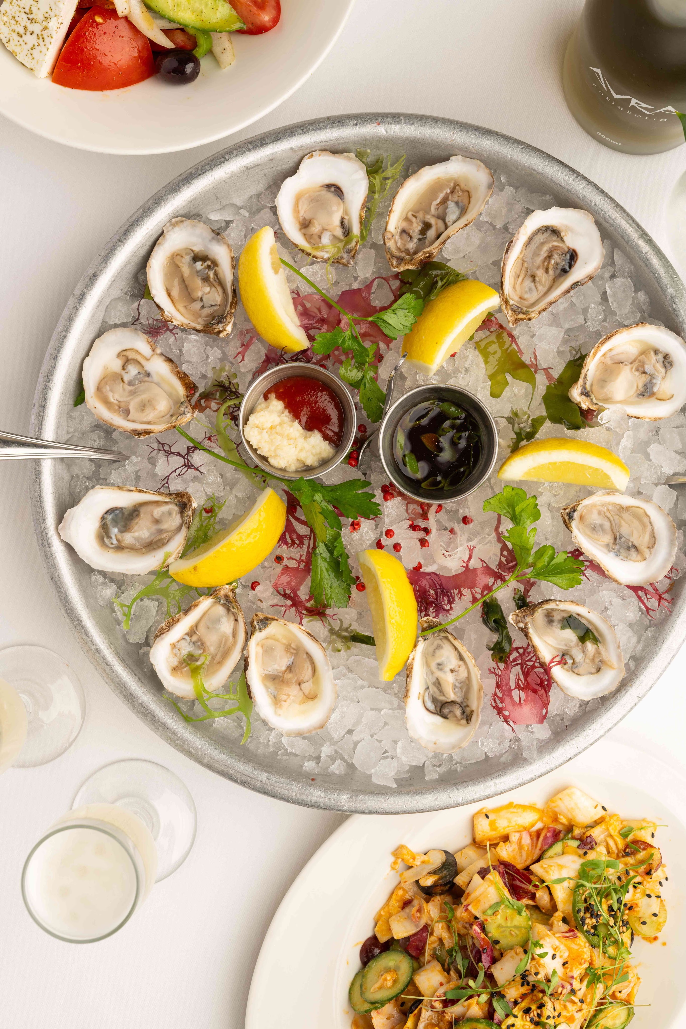 A circular platter filled with oysters, garnished with lemon wedges and accompanied by side dishes.
