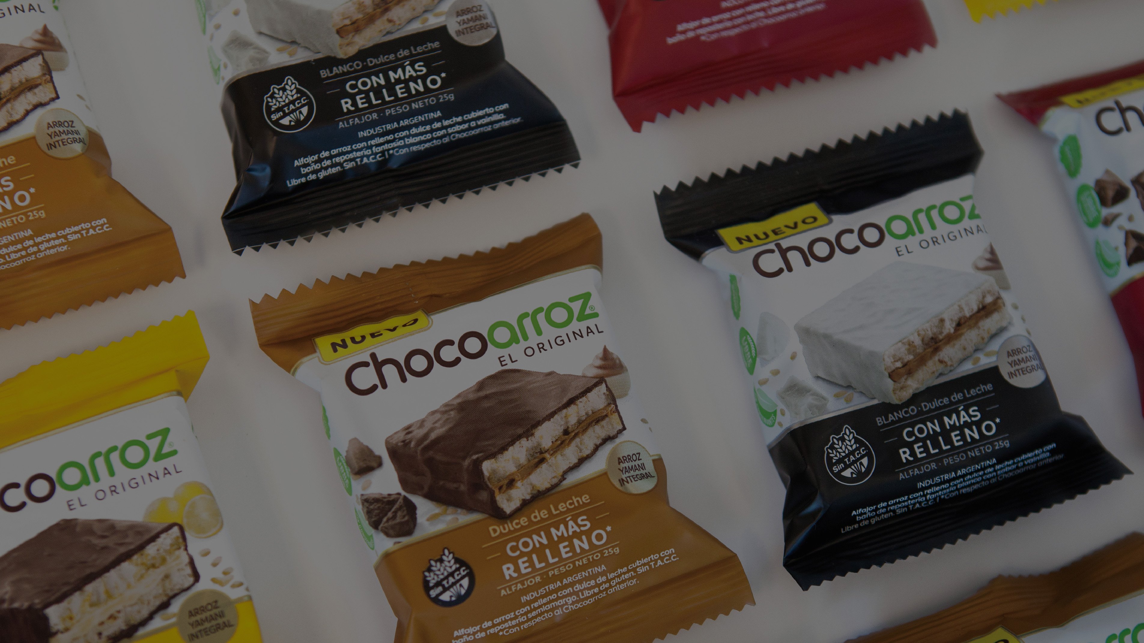 Close-up of various Chocoarroz snack packages in diverse colors and flavors, like dulce de leche and chocolate, arranged on a white surface.
