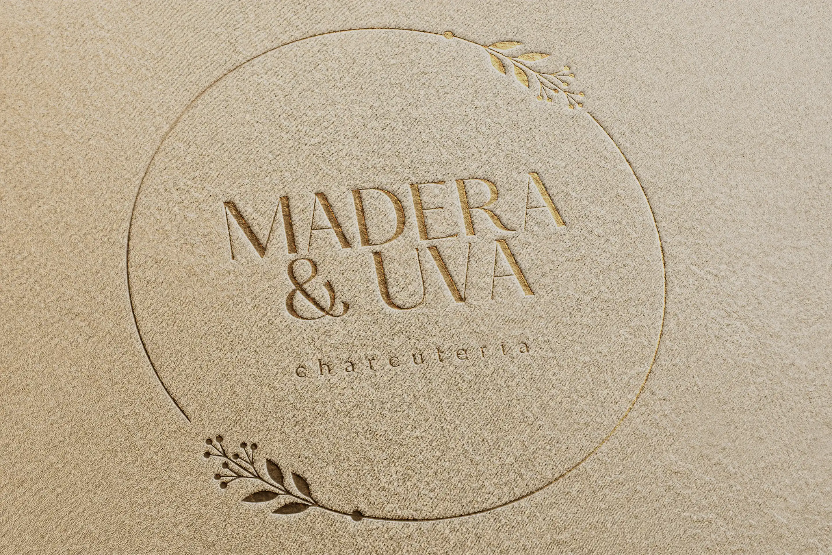 Logotipo de "Madera y Uva" en relieve dorado sobre papel texturizado