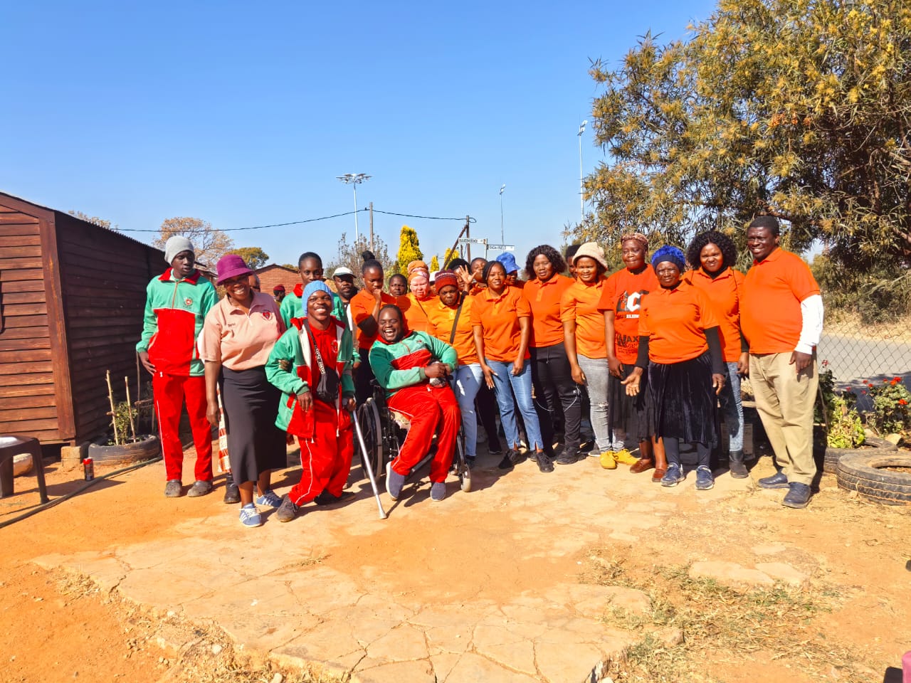 A smiling woman with her arms crossed, standing against a dark green background. She has long, dark hair.