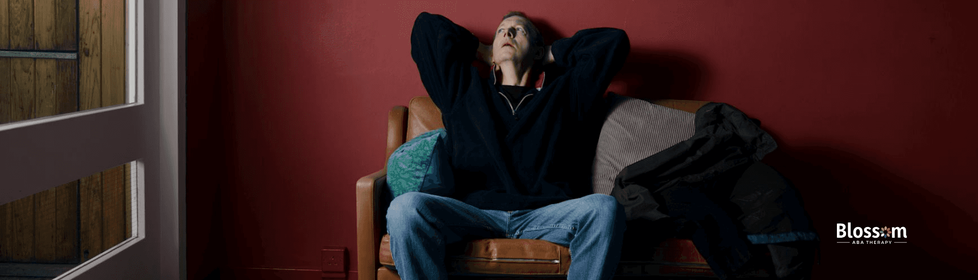 An adult with autism sitting on a couch in room, looking up and showing autistic shutdown symptoms.