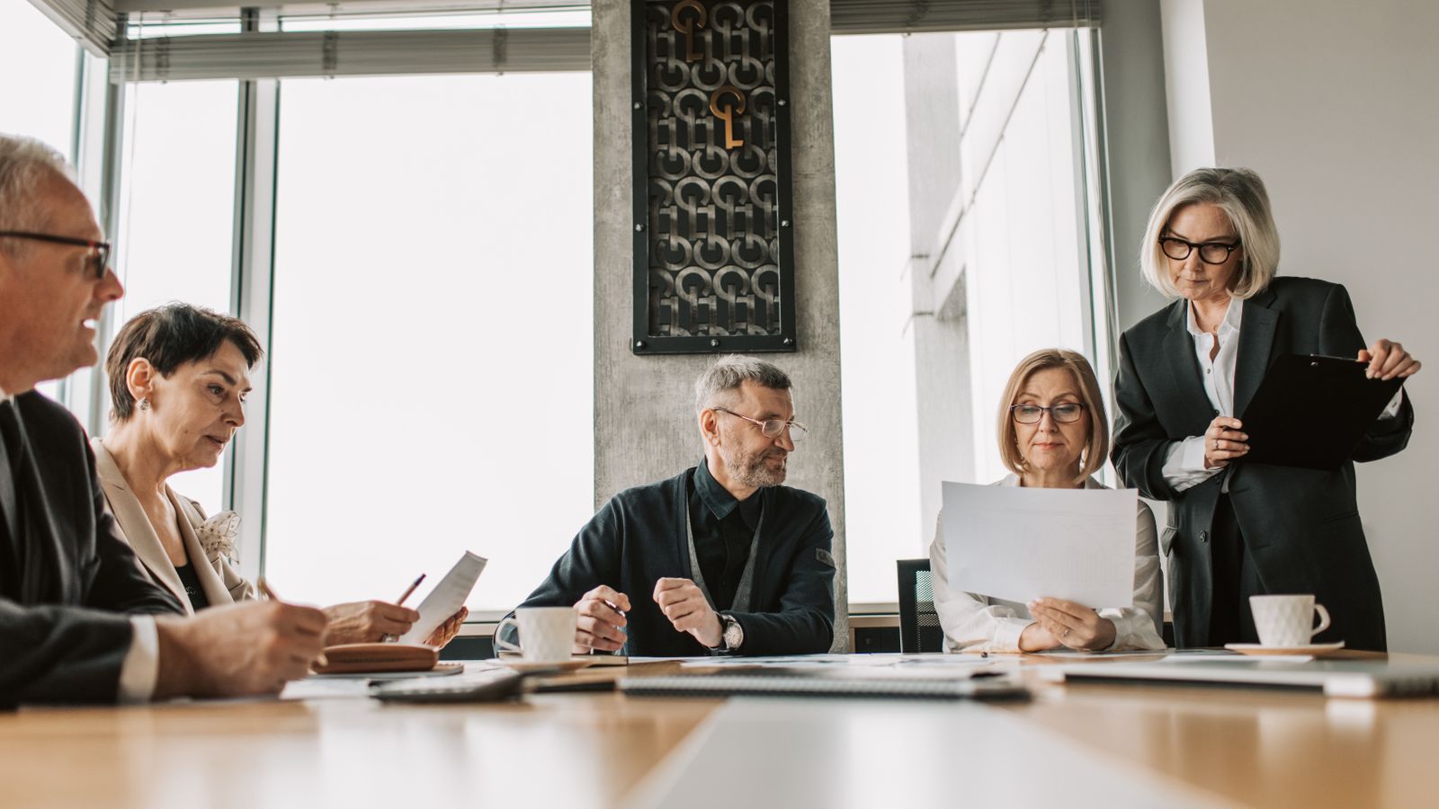A buying committee of five executives reviewing documents and charts around a boardroom table