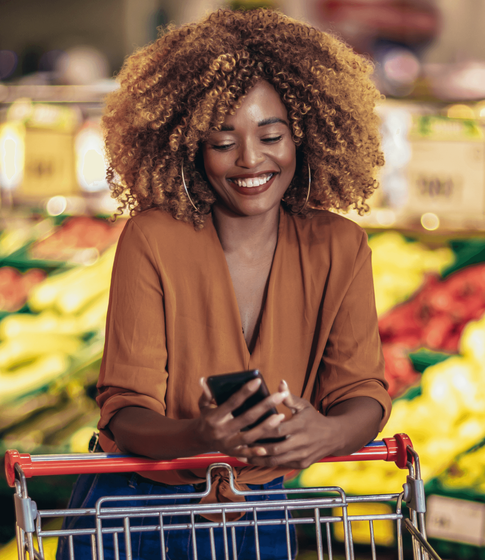 Woman smiling looking at her phone while standing in a supermarket.