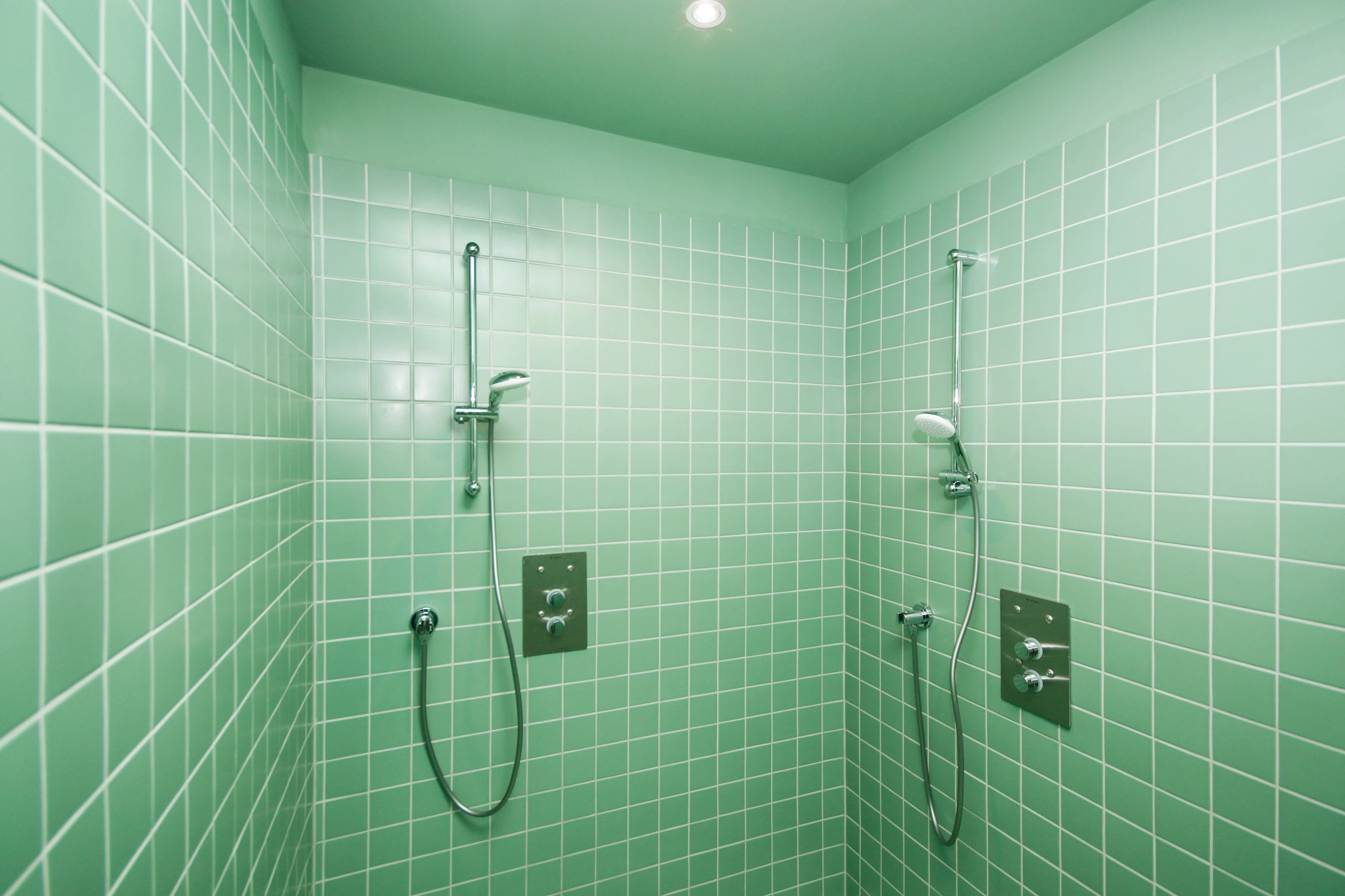 Shower area at CYCLA fully tiled in mint green with two chrome rain showers and a green-painted ceiling.