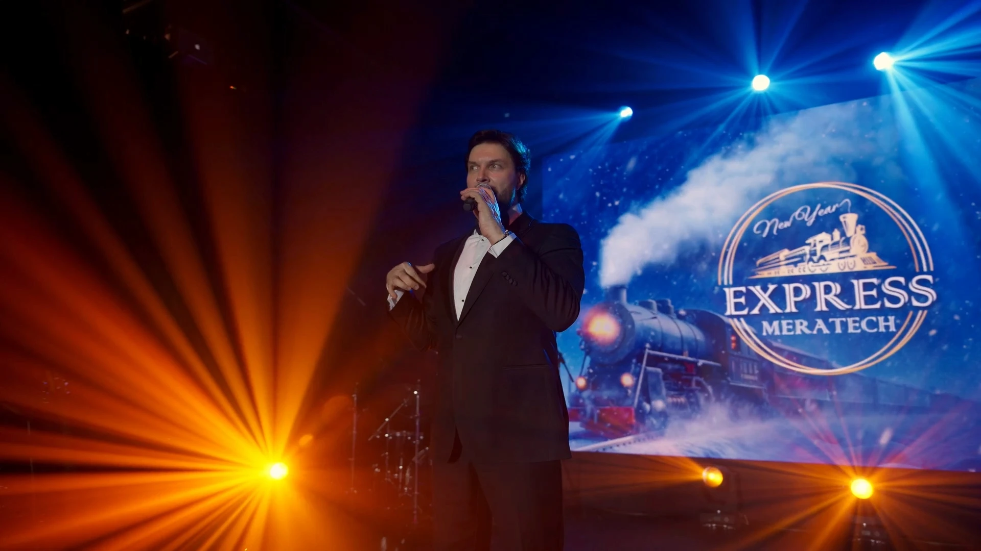 A man standing on stage with a microphone in orange light