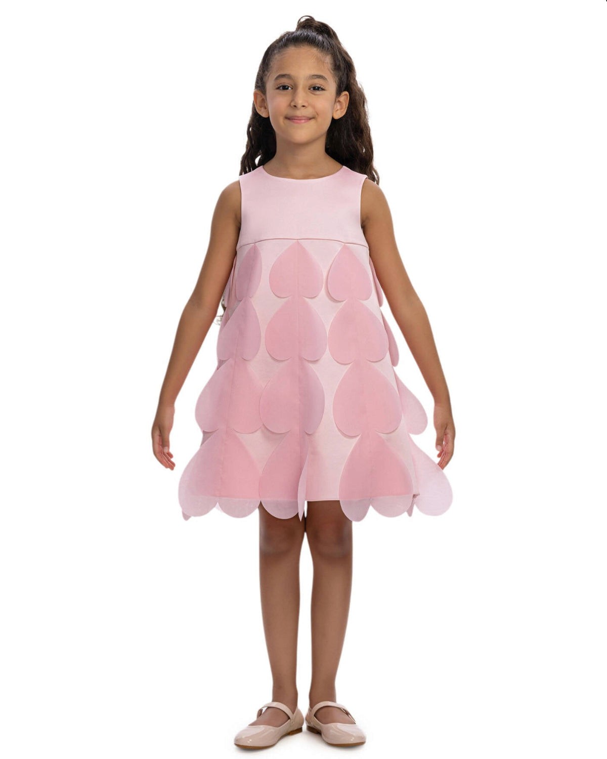 Young girl wearing a pink dress with scalloped layers on a white background