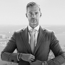 Professional portrait of a woman with blue eyes, dark brown hair, and a black blazer, set against a plain background.