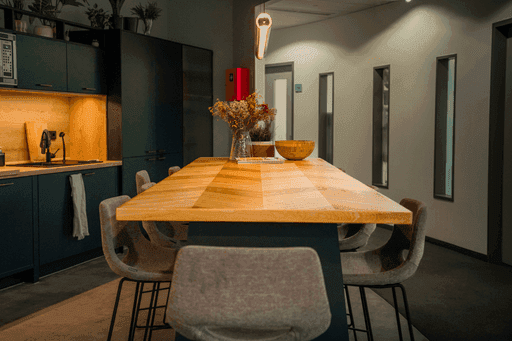 Moderner Essbereich mit langem Holztisch, grauen Stühlen und dunkler Küchenzeile im Hintergrund