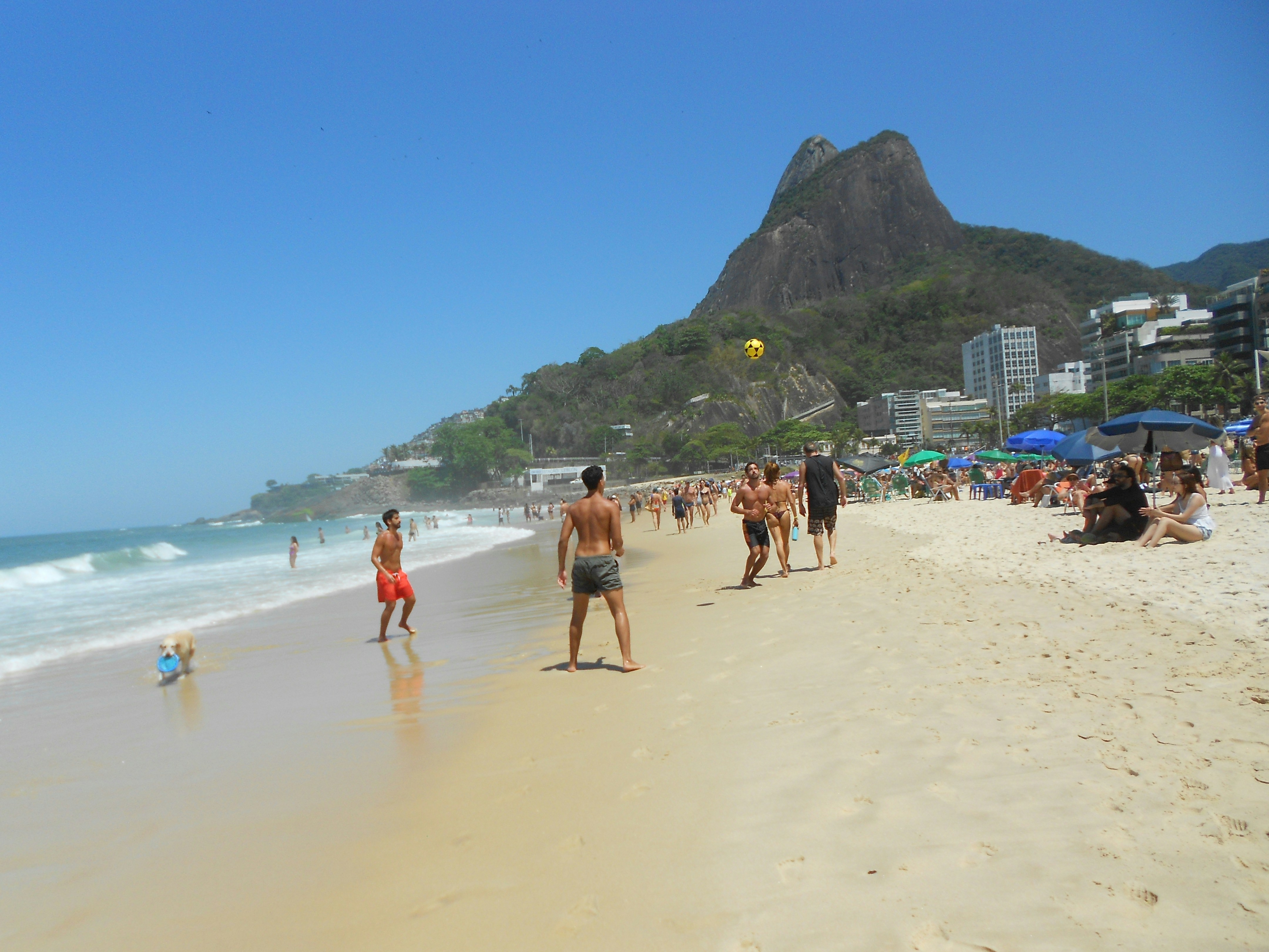 People playing volleyball on a sunny beach with mountain backdrop