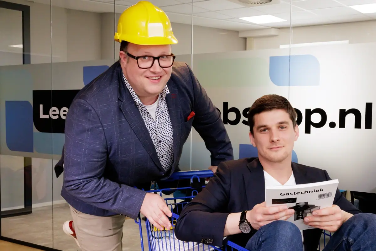 Twee collega's van MBOwebshop.nl met een winkelwagen in hun kantoor