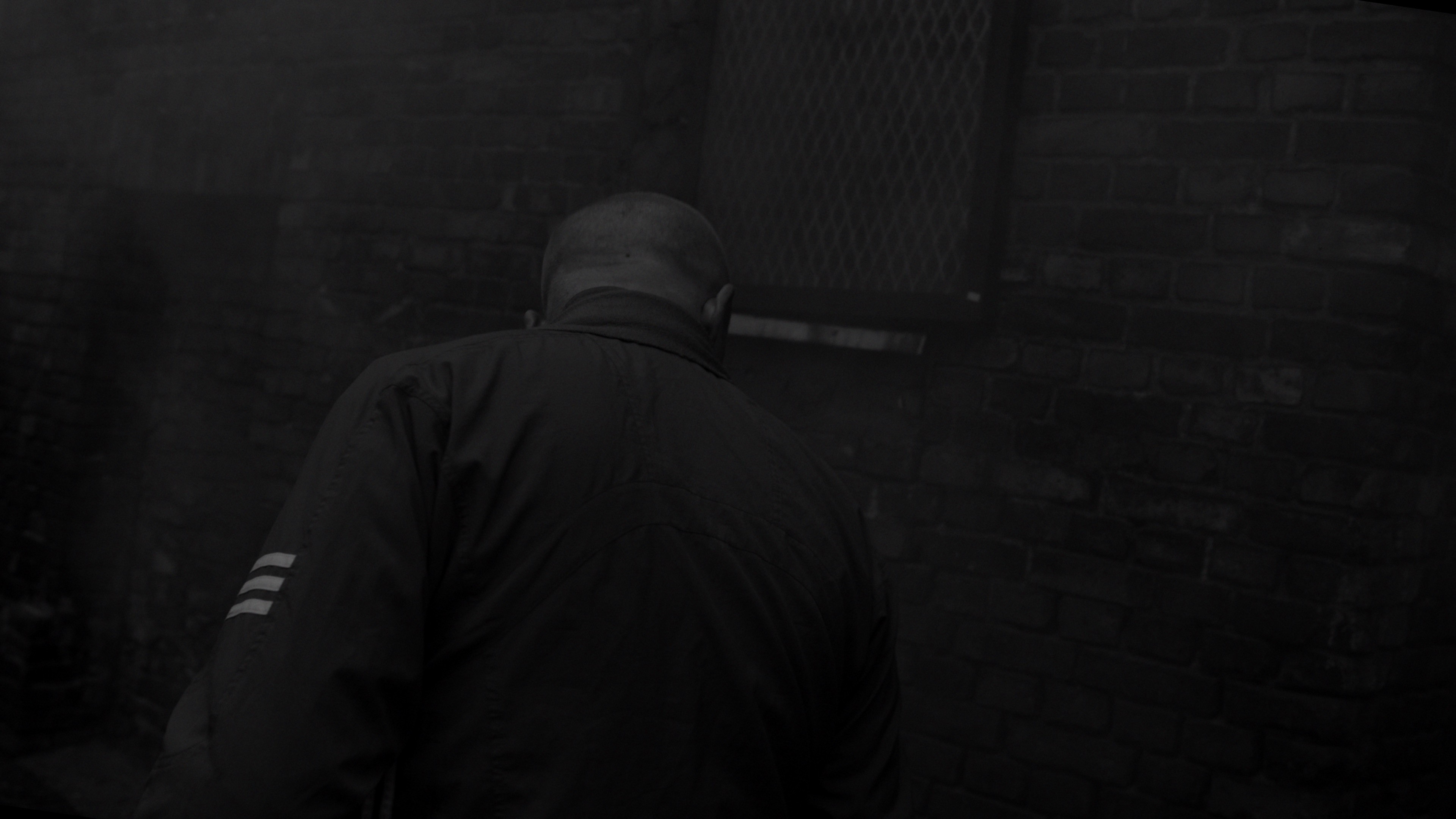 Rear view of a football hooligan walking through an abandoned courtyard, gritty B&W style.